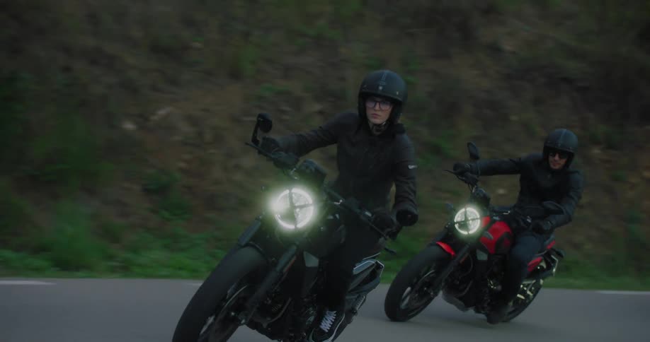 Group of motorcyclists on a twilight ride along a hilly road with their headlights illuminating the path
