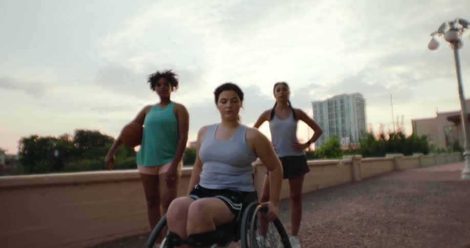 Two women standing next to another woman sitting in a wheelchair all posing for a photo with a serious expression