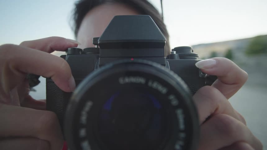 A closeup of a persons hands taking pictures with a film camera with a large lens (POV)