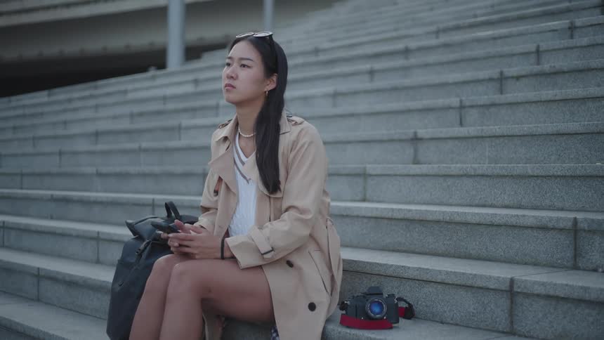 A woman sitting on concrete stairs looking at her cellphone with her camera behind her