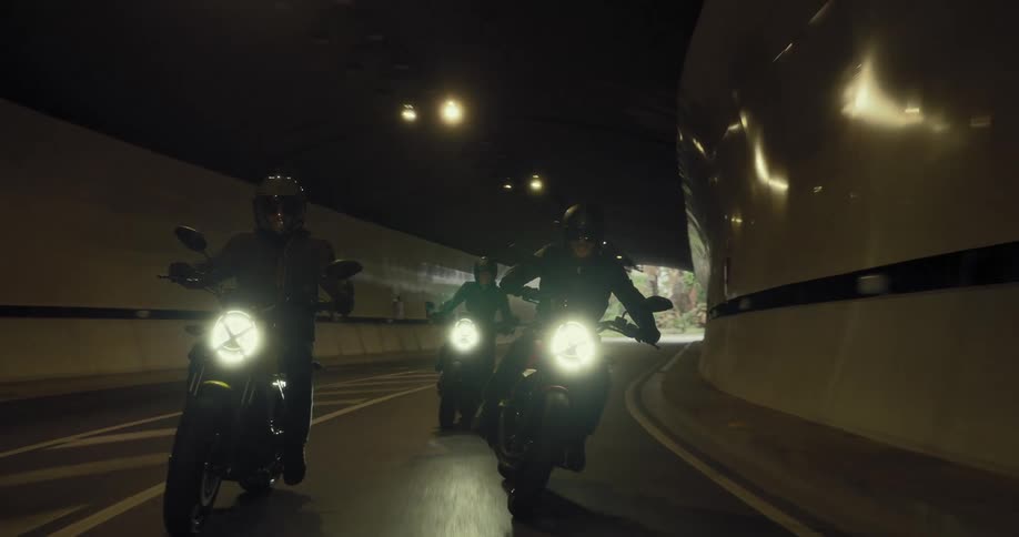 Three men on bicycles riding through a tunnel on a roadway together