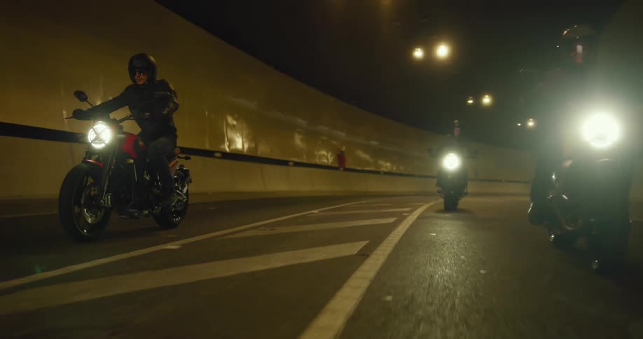 Motorcyclists ride through a graffiti marred tunnel and emerge during a summer day