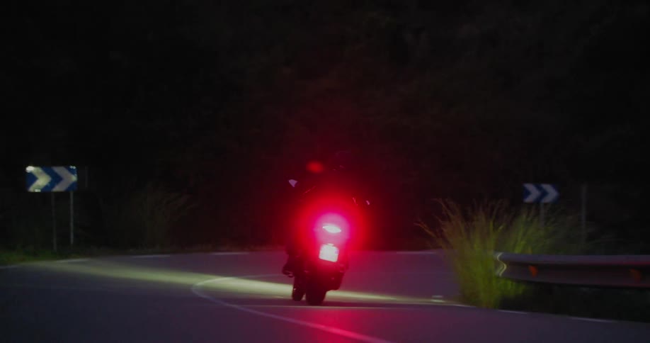 A motorcycle making a turn on a darkening asphalt street and the motorcycle has a red light on the back