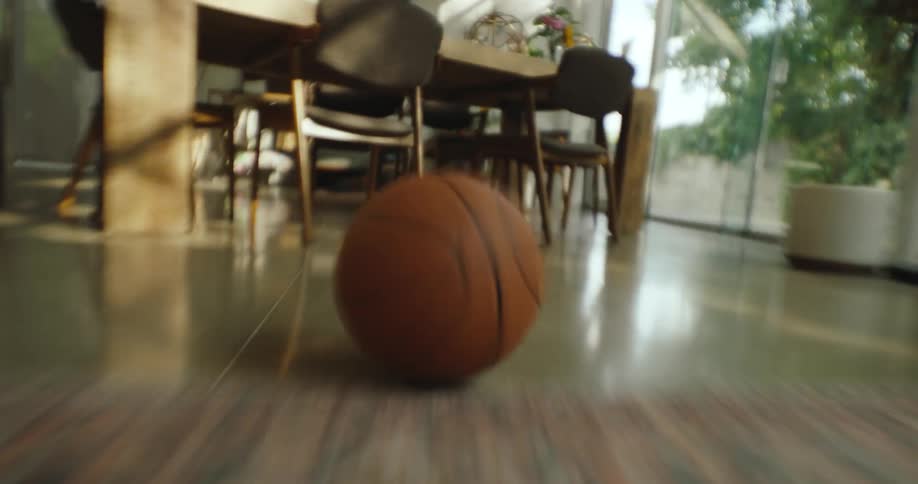 Time lapse of a basketball rolling through the living room and under a table