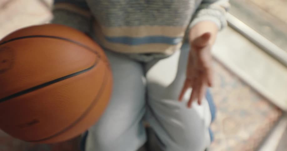 Close up of a person tossing a basketball between their hands as they sit in a wheelchair