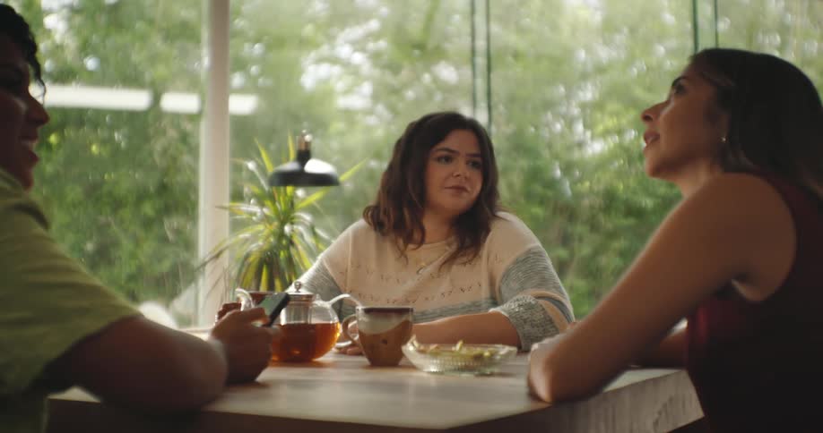 A group of three female friends who are around a table with some food and they are talking