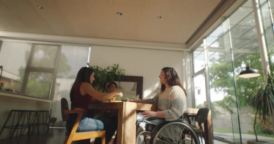 Friends seated at a wooden table one in a wheelchair engaged in conversation