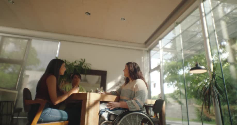 Three people are sitting at a table by a large window chatting and enjoying each others company