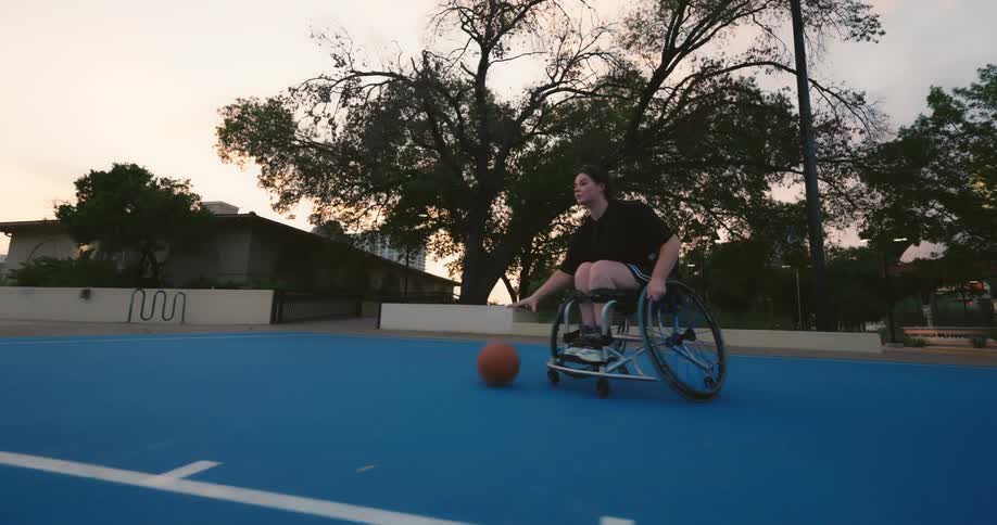 Female special athlete dribbles the basketball while maneuvering her wheelchair on an outdoor basketball court