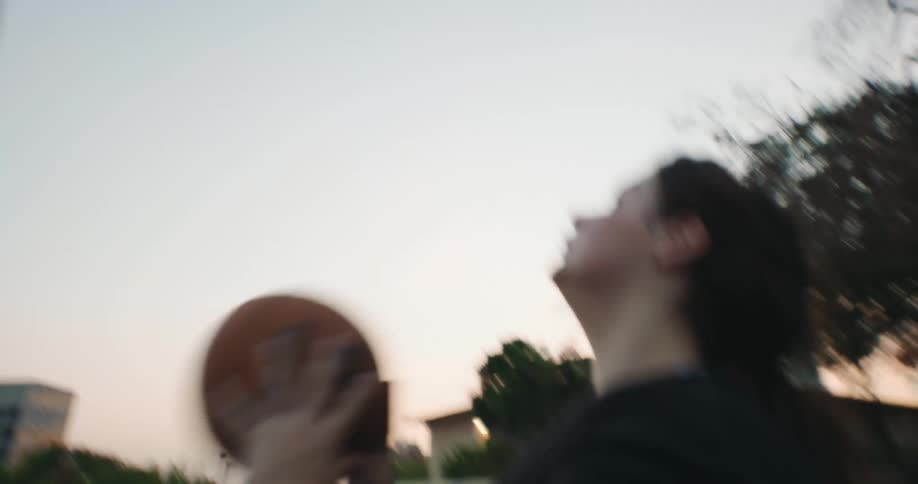 Woman wheeling around in her wheelchair playing basketball on an outdoor court at dusk