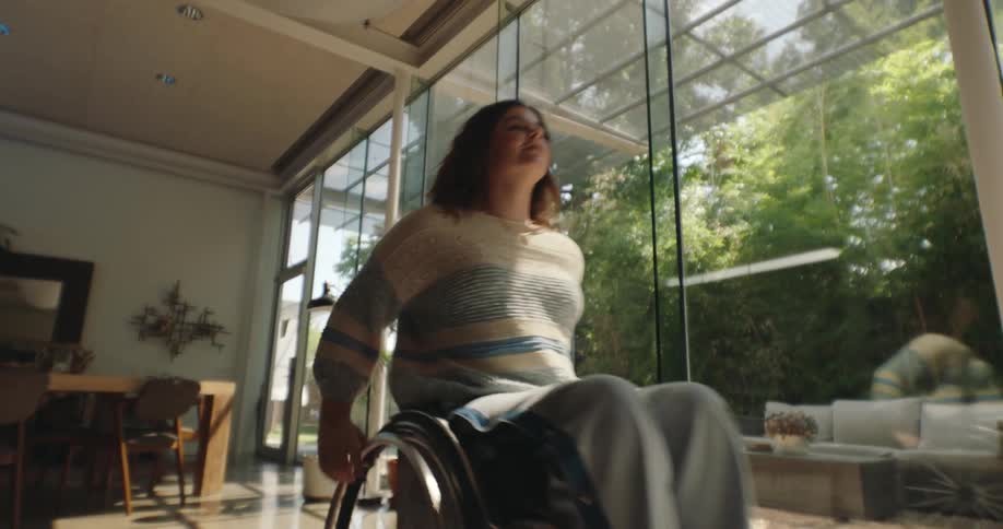 A woman in a wheelchair moving across her living room in front of large glass windows letting the light in