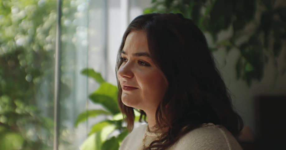 A teenage female smiles as she sits in a room by windows