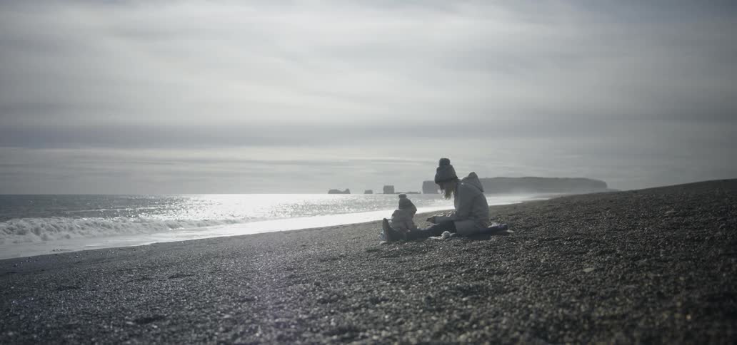 A woman and young child sit on a beach on a chilly day