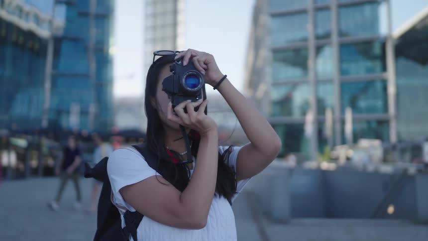 A woman photographer holding a camera up to her face taking pictures of the city and buildings around her
