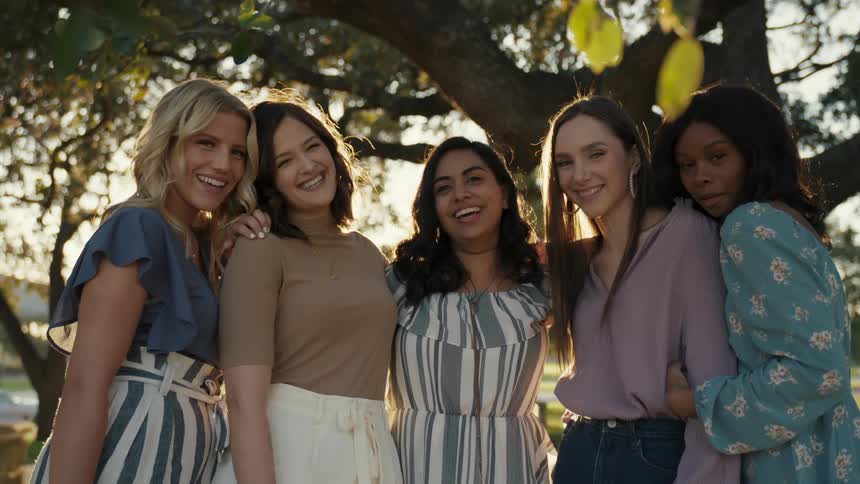 Five women stand together and smile and laugh underneath a tree