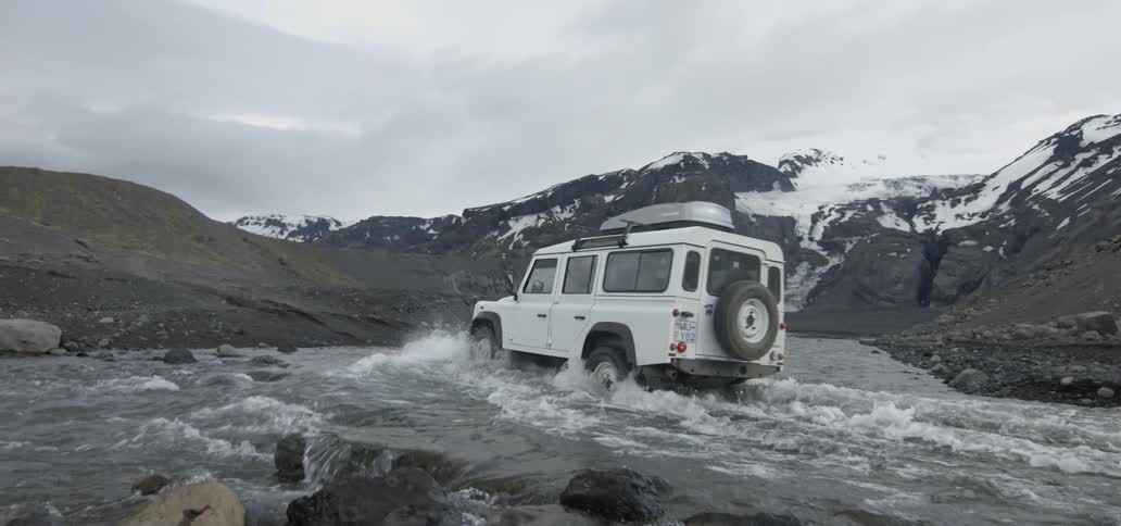 A vehicle drives across a river in the mountains