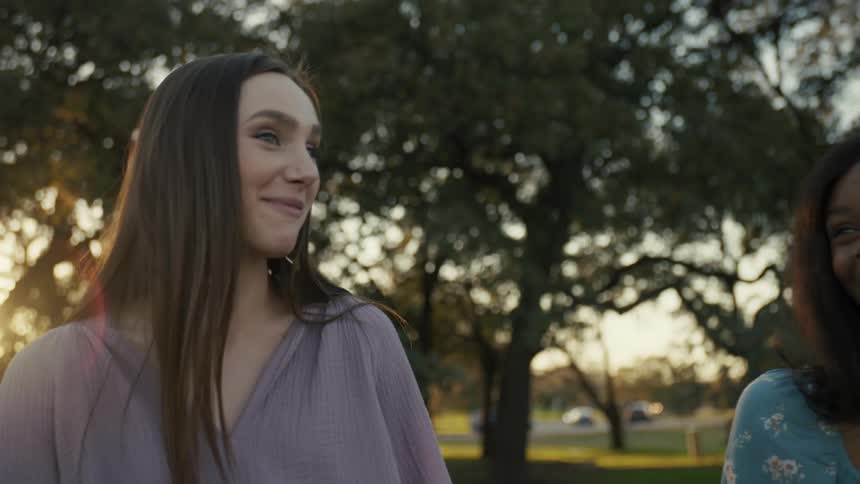 Two happy teenage girls outdoors during sunset with sunlight filtering through trees in the background
