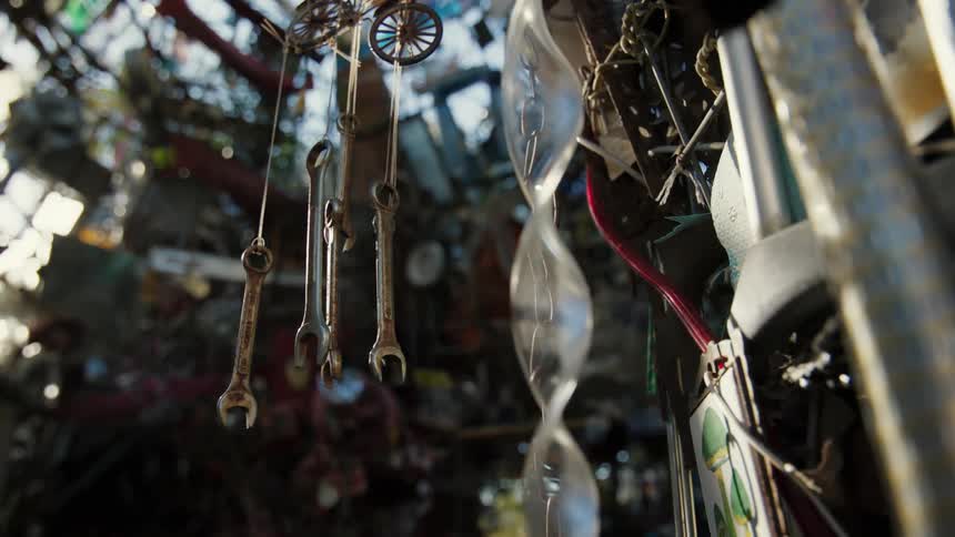 A wind chime made of wrenches hangs against a background of assorted junk