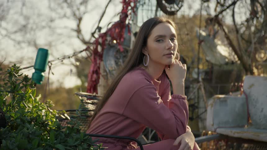 A young woman sitting outdoors with their chin resting on their hand in front of an array of cluttered objects
