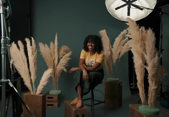 A woman laughs and smiles while modeling from a stool in a studio