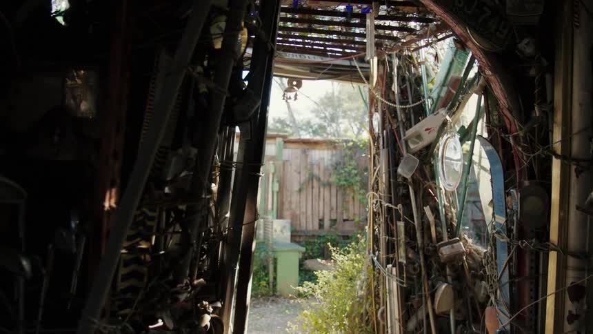 A structure filled and built out of junk leads to a backyard garden
