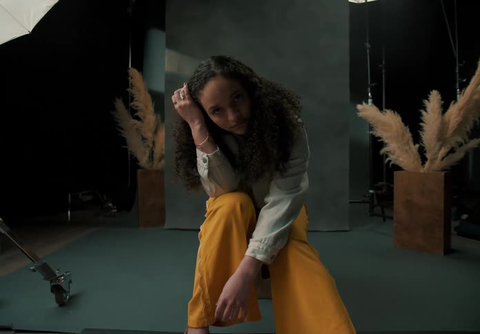 A young woman sits in a room with lighting for photography set up