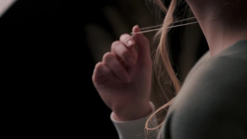 Close up of a womans neck and chin as she plays with a necklace around her neck