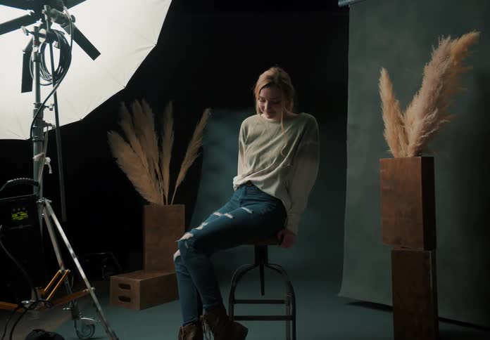 A blonde haired woman gets ready to model for a photo while sitting on a stool