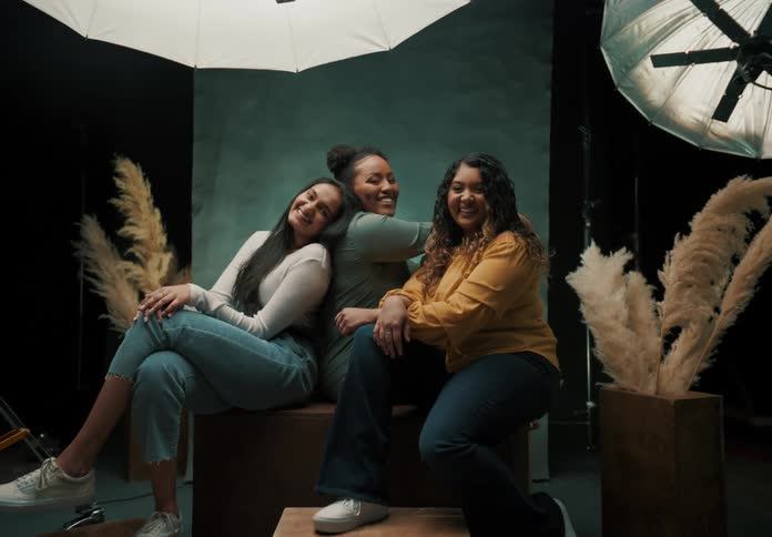 Three young women laugh and smile while sitting in a photography studio