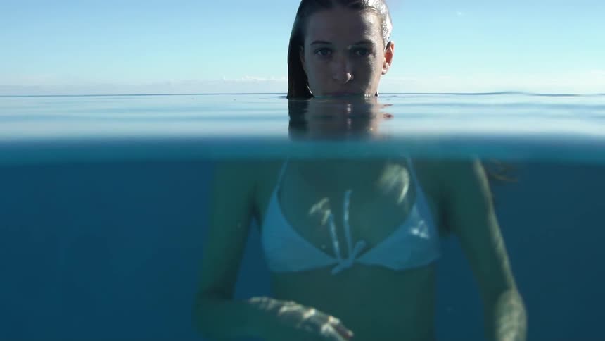 A young woman in a white bikini has her face out of the water and her body is underwater and she is staring straight ahead