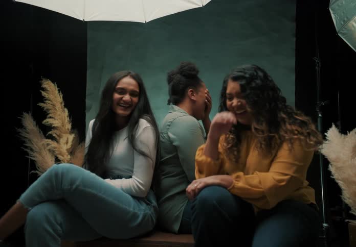 Women wearing fashionable clothes laugh and talk while posing in a photography studio