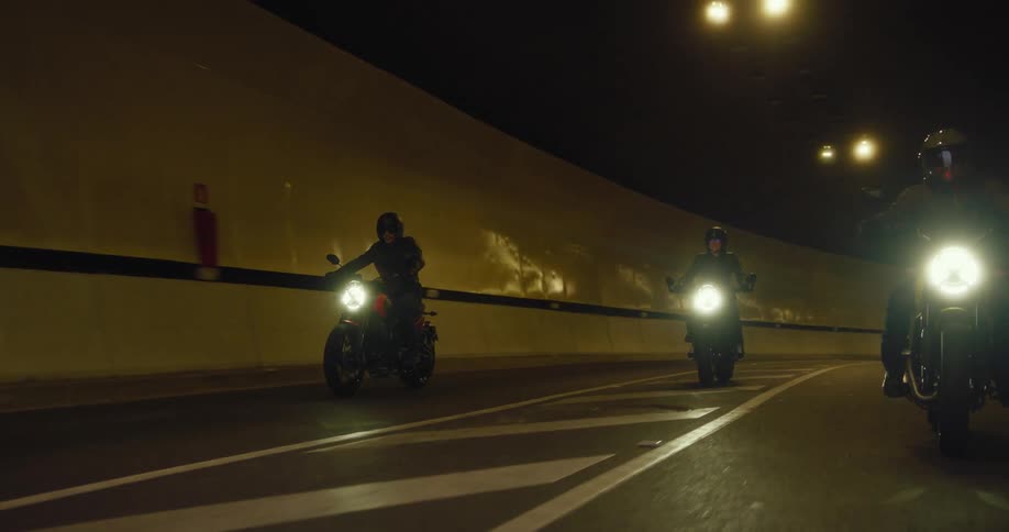 Three men ride motorcycles from a tunnel on to the city street