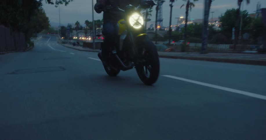 A motorcyclist with a yellow motorcycle driving on an asphalt road and next to it another street with only cars passing by