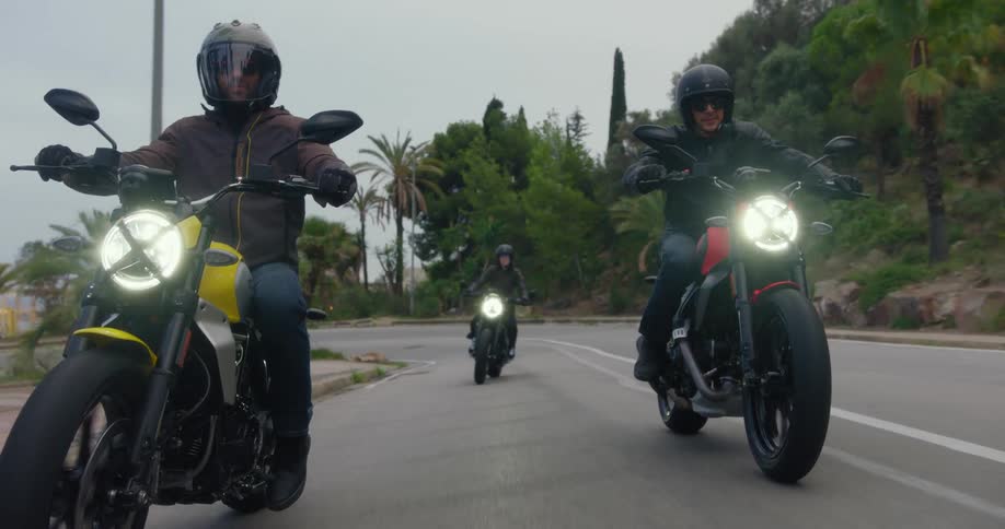 A group of three bikers in black clothes riding yellow and red sports bikes on an asphalt street