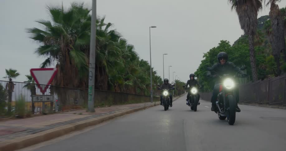 Motorcyclists ride their motorcycles on the frontage road bordering a traffic filled freeway on an overcast day
