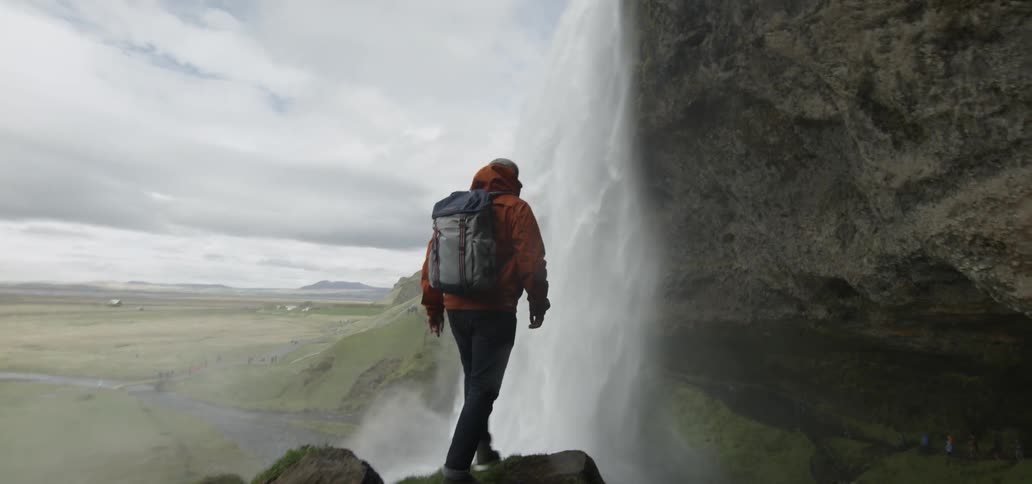 Man standing at the edge of a cliff watching a waterfall