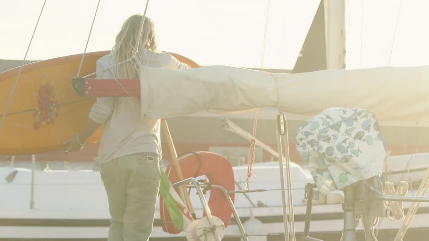 A man handing an orange surfboard to another man standing on a boat who takes it and sets it down