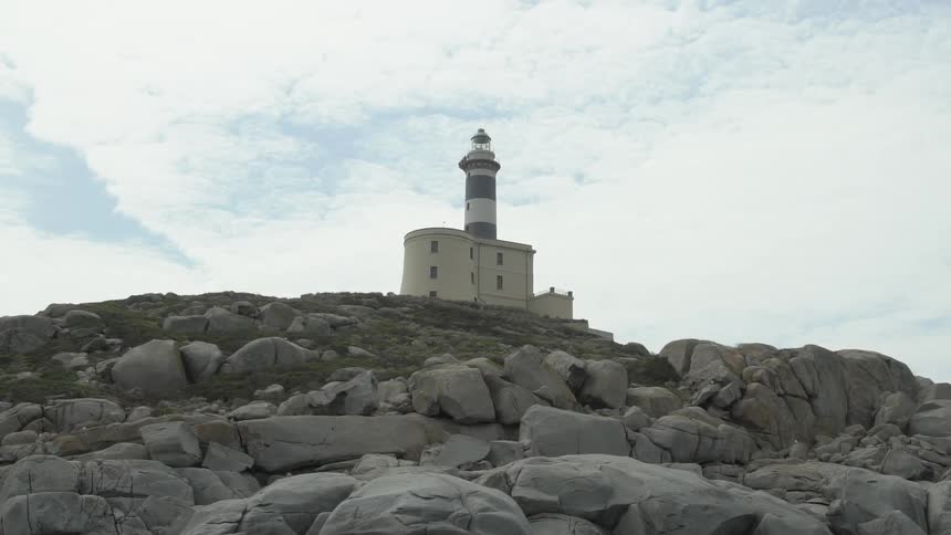 A lighthouse on the top of a hill of rocks on bright day with clouds in the sky