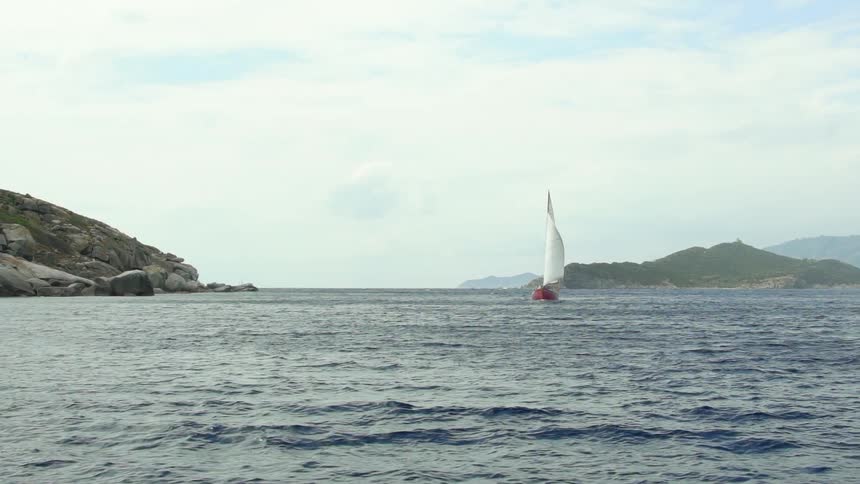 A sailboat sailing in a sea near a coast full of rocks