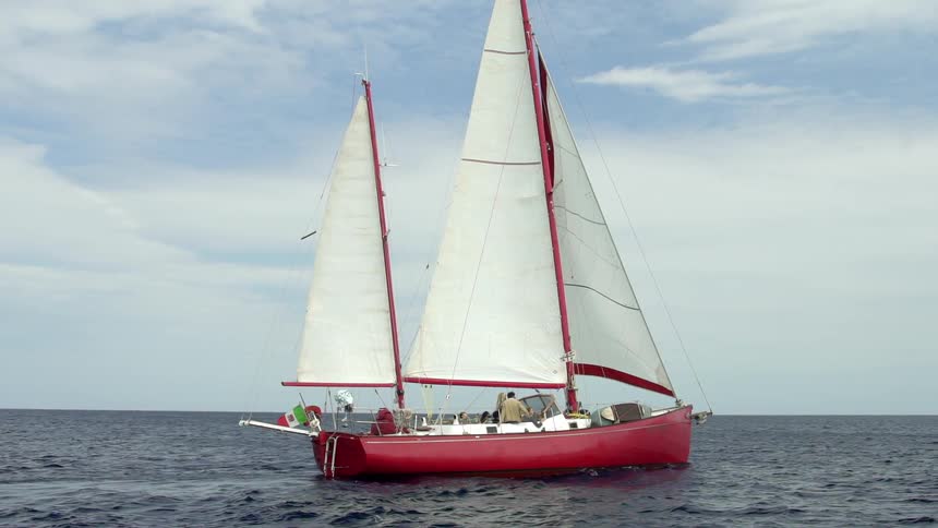 People on a red sailboat moving across the ocean