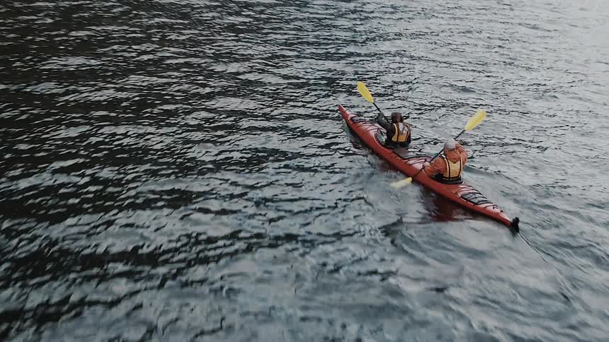 Two people paddling a canoe in the middle of a lake being filmed by a drone