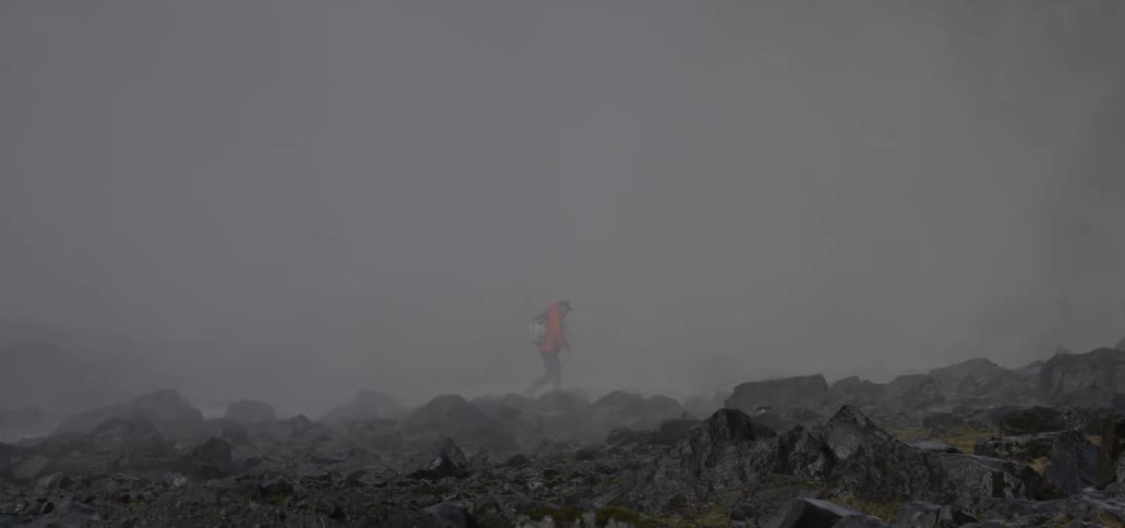 A male hiker is walking across a rocky landscape filled with smoke