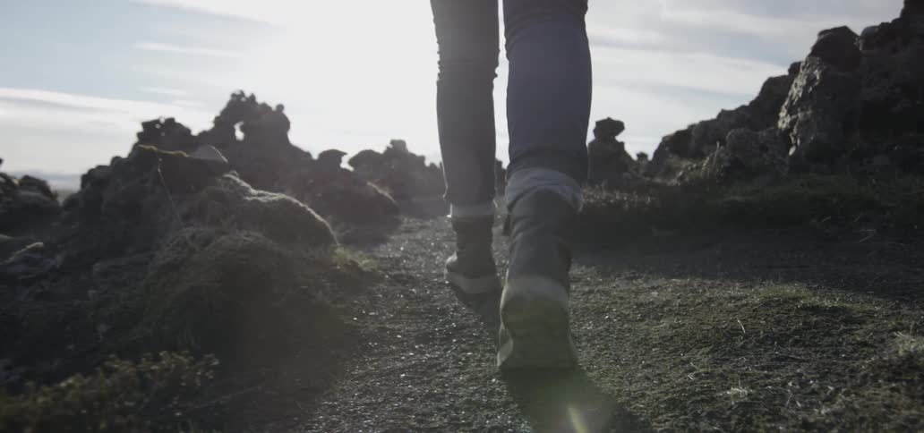 A person walks over a dirt path on a sunny day