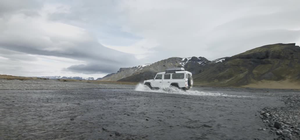 A vehicle drives through a wide creek to the other side
