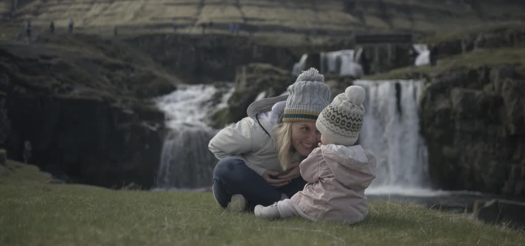 A man and woman sit on a grassy hill near a waterfall