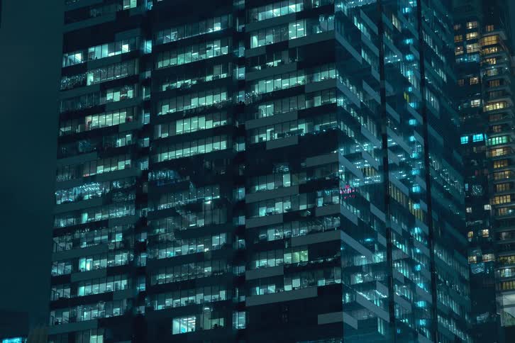 A residential building with the lights of the apartments turning on as night turns to day