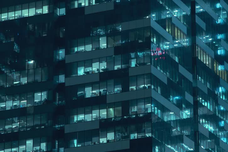 The exterior of modern high rise buildings at night with illuminated windows turning on at night