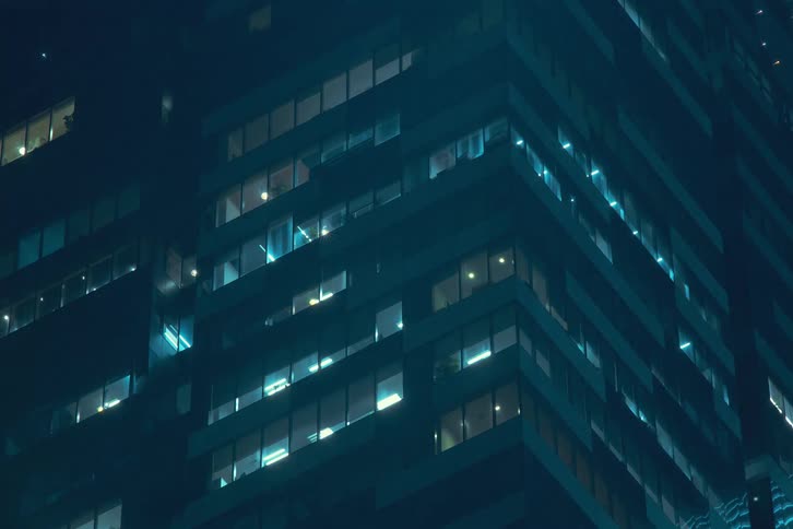 The exterior of modern high rise buildings at night with illuminated windows blinking and flashing