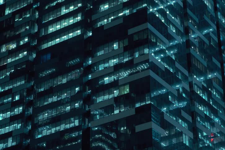 A time lapse of an office building in a city at night with lights on different levels turning on