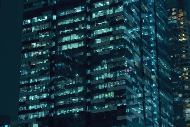 A time lapse of the side of an office building at night with the lights in the windows on different levels are turning on